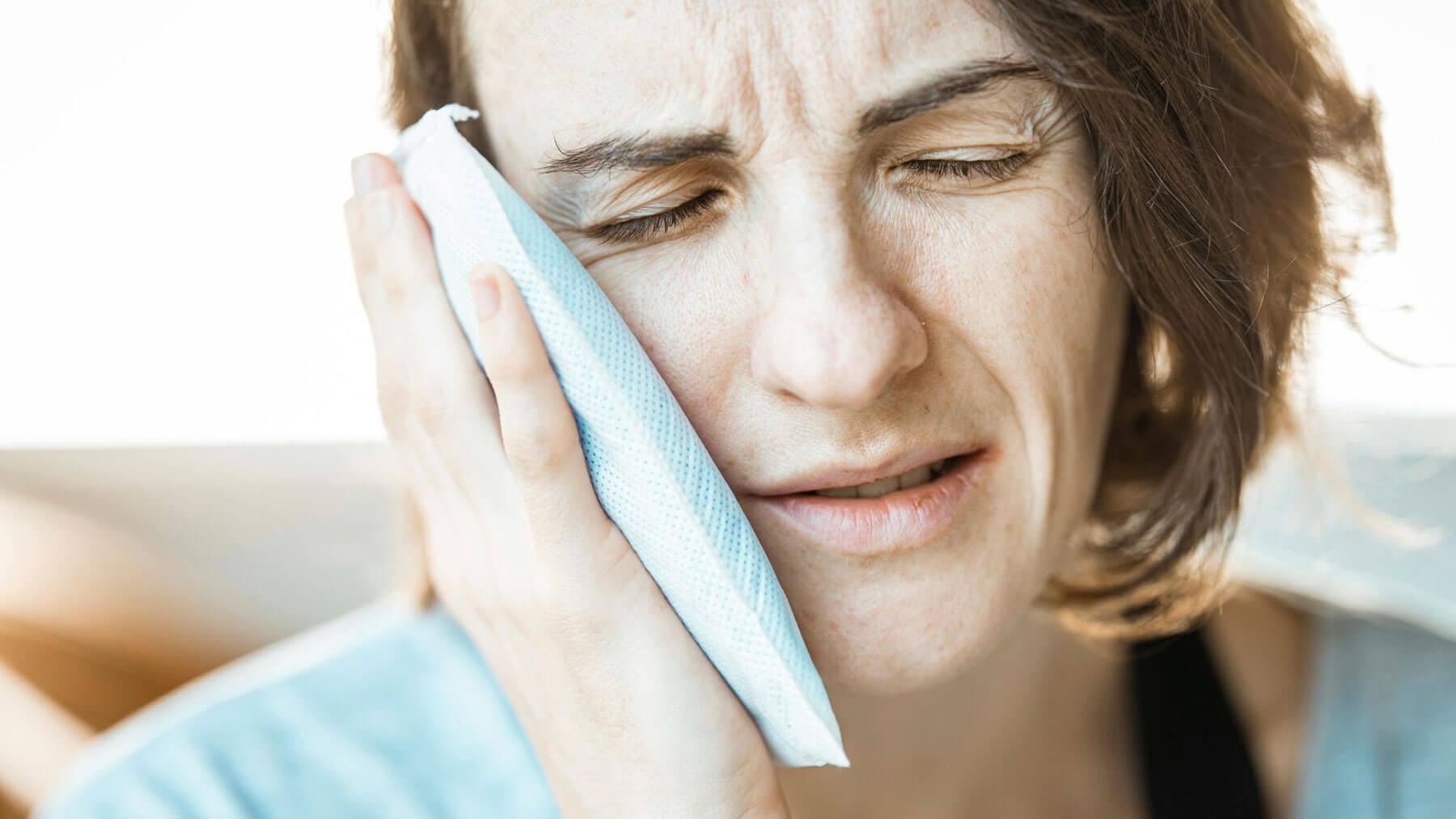 Patient holding ice pack after wisdom teeth removal to reduce swelling